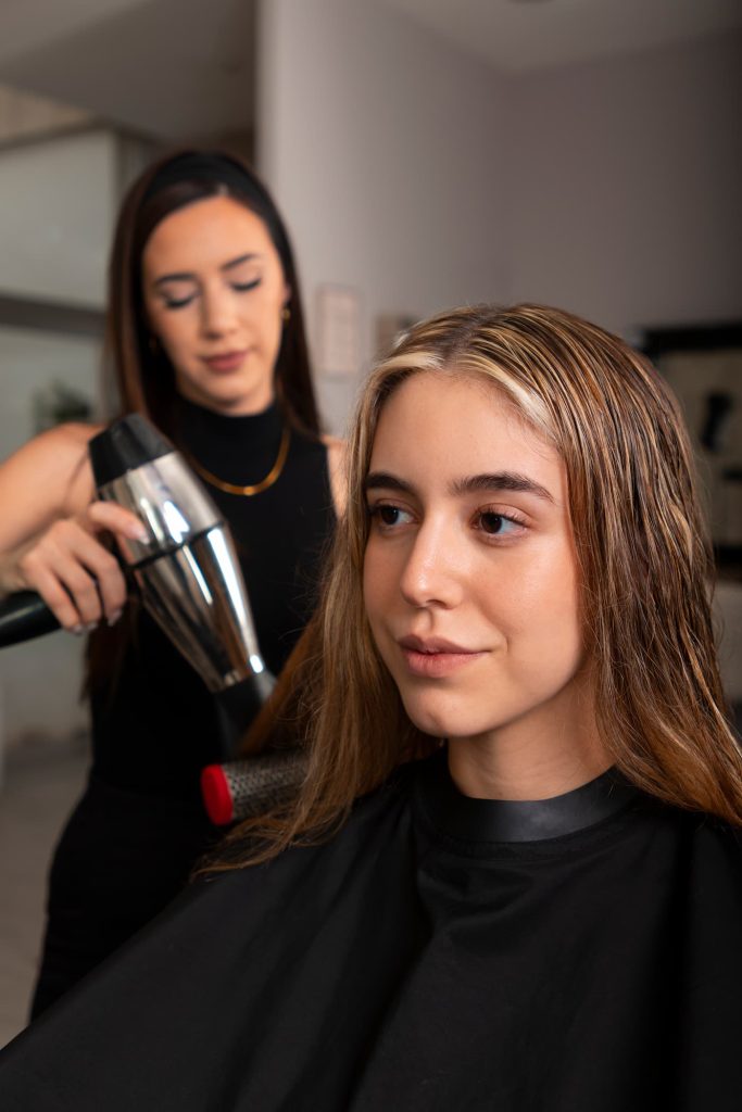 Fryzjer suszący włosy klientce w salonie fryzjerskim