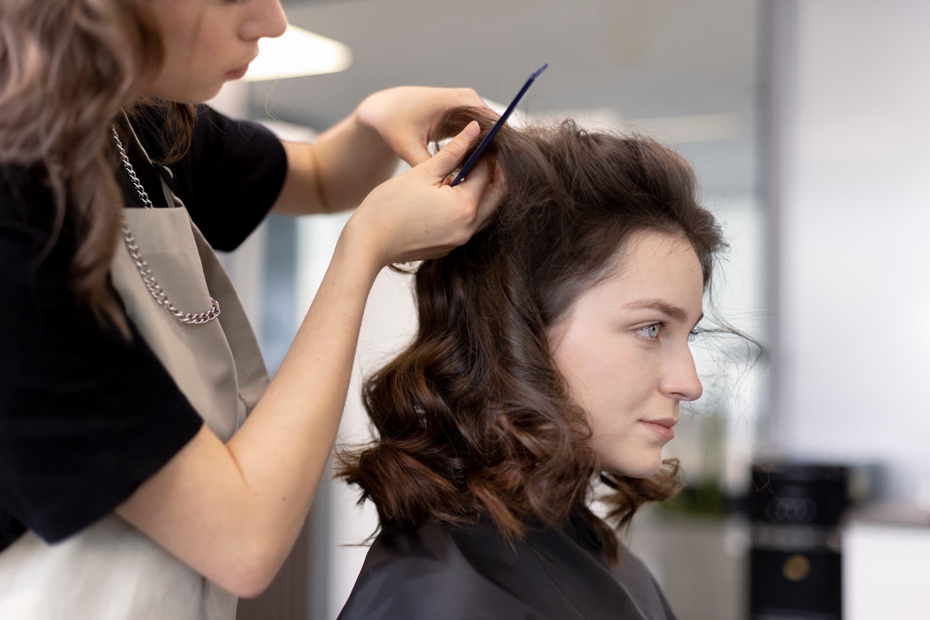 Fryzjer modeluje i układa włosy klientki podczas stylizacji w salonie fryzjerskim.