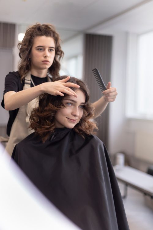 Fryzjer wykańcza modelowanie włosów klientki grzebieniem w salonie fryzjerskim.