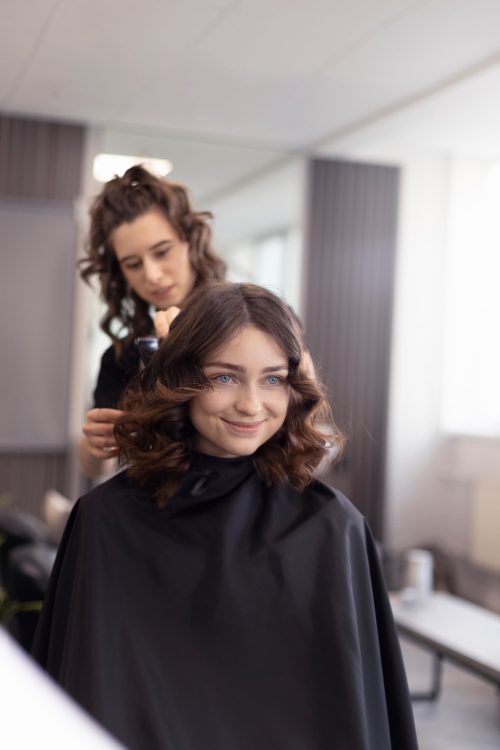 Klientka z ułożonymi falami podczas końcowego modelowania włosów w salonie fryzjerskim.