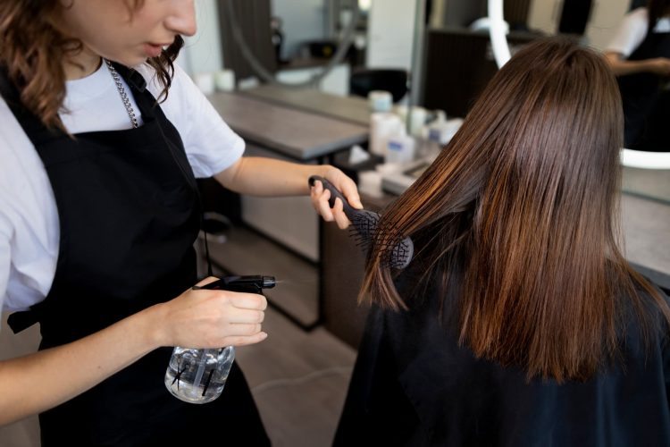 Fryzjer modeluje długie włosy klientki szczotką podczas stylizacji w salonie fryzjerskim.