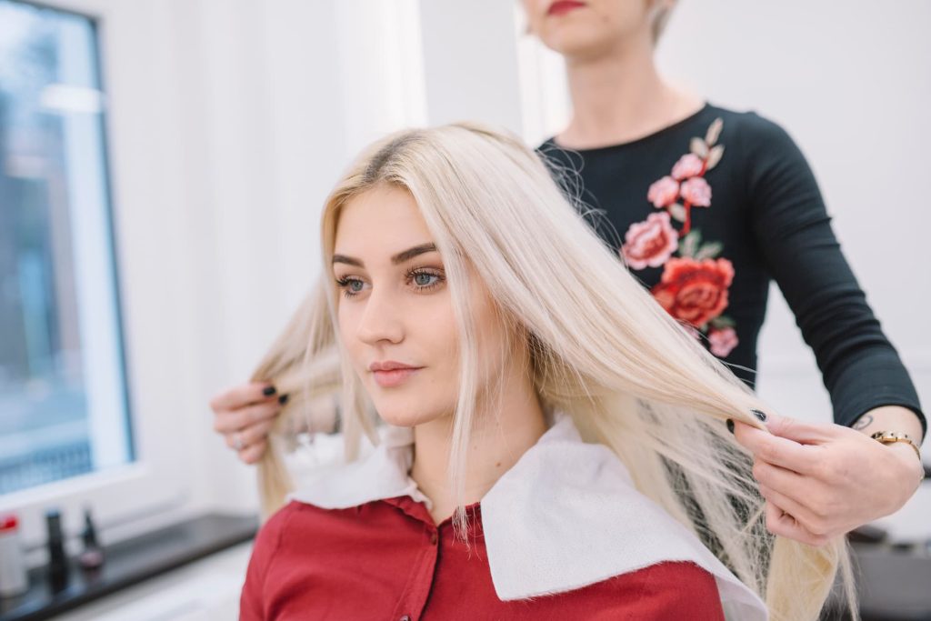 Fryzjerka ocenia efekt koloryzacji i kondycję blond włosów klientki.